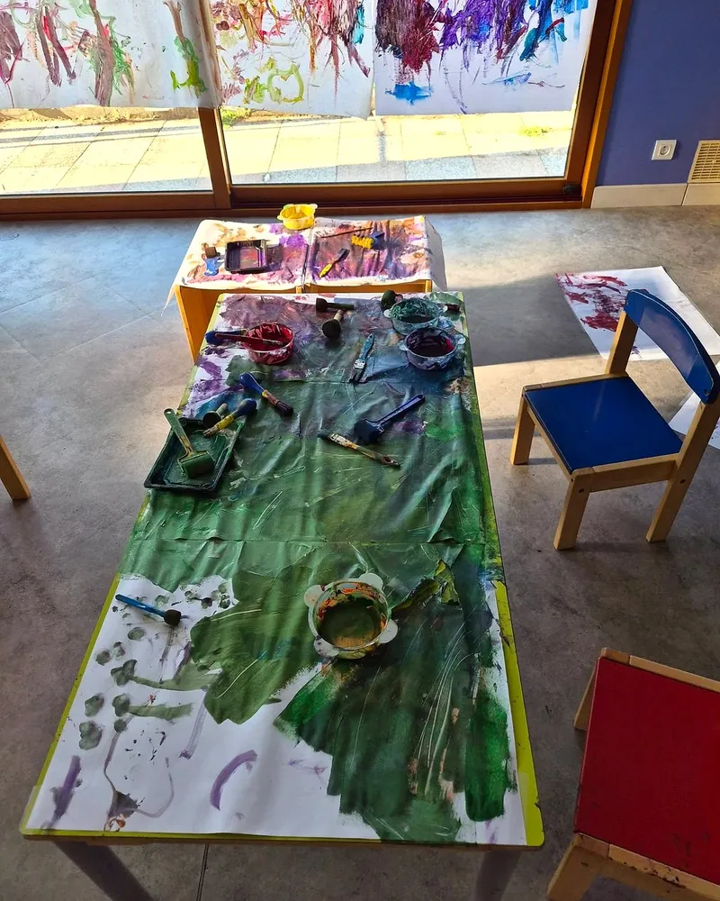 Table recouverte de papier, pots de peinture, rouleaux et pinceaux, avec des chaises enfant