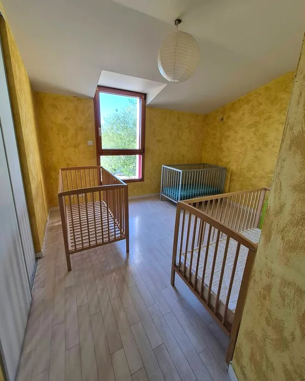 Chambre aux murs jaunes avec trois lits à barreaux et une grande fenêtre